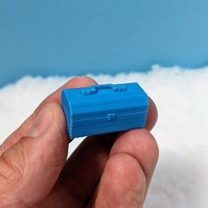 Op de afbeelding: Een kleine blauwe gereedschapskist met een handvat en een sluiting. De gereedschapskist is gemaakt van plastic en heeft een getextureerd oppervlak.
