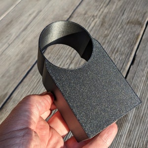 Könnte beinhalten: Ein schwarzer 3D-gedruckter Getränkehalter mit einer runden Öffnung. Der Halter ist aus strukturiertem Kunststoff.