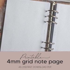 Może przedstawiać: Otwarty planer w formacie A5 z kartką z notatkami w kratkę 4 mm. Papier w kratkę jest biały z jasnoszarym wzorem kratki. Planer jest ze skóry brązowej ze srebrnymi metalowymi pierścieniami. Tekst na zdjęciu brzmi "Printable 4mm grid note page".