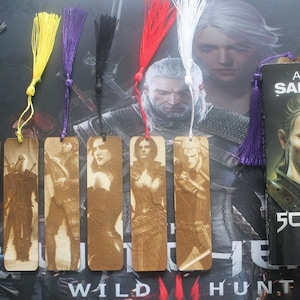 Peut inclure: Cinq marque-pages en bois représentant des personnages de la série de jeux vidéo The Witcher. Chaque marque-page présente un personnage différent et un pompon de différentes couleurs. Les marque-pages sont affichés sur un fond avec le texte "Wild Hunt".