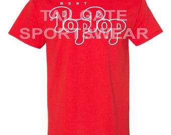 May include: Red short-sleeved t-shirt with white text that reads "Best Tailgate Pop Pop Ever"