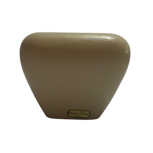 May include: A beige, ceramic vase with a rounded top and a triangular base. The vase has a smooth, glossy finish. A small, rectangular sticker with the text "Haggen Floral" is on the front of the vase.