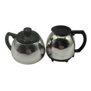 May include: Two vintage silver-colored coffee pots with black handles and lids. The pots have a rounded shape and are designed for brewing coffee. The lids have a small knob on top for easy removal.