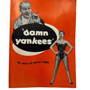 Puede incluir: Un póster naranja vintage de la comedia musical Damn Yankees. Presenta una ilustración en blanco y negro de un hombre con un cigarro sobre un óvalo negro con el texto blanco "damn yankees" y una mujer con un leotardo negro debajo.