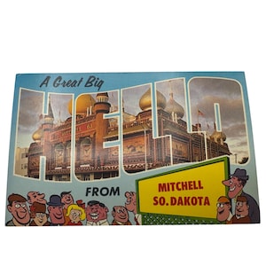 Könnte beinhalten: Eine Vintage-Postkarte mit einer Cartoon-Illustration eines Gebäudes mit dem Wort "HELLO" in großen Buchstaben. Das Gebäude ist mit bunten Flaggen geschmückt und trägt ein Schild mit der Aufschrift "Mitchell, So. Dakota". Die Postkarte zeigt auch eine Gruppe von Cartoon-Menschen mit lächelnden Gesichtern.