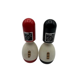 May include: Two vintage salt and pepper shakers. One shaker has a red top and the other has a black top. Both have a white egg-shaped base with three small brown rectangles. Each shaker has a label that says "CYPRUS" with a fish graphic.