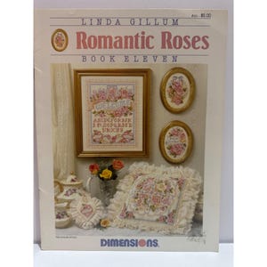 May include: A craft book titled "Romantic Roses Book Eleven" by Linda Gillum. The cover features cross-stitch designs of roses, including a framed "Welcome" sampler and two oval framed pieces. A pillow and other items with rose designs are also shown.