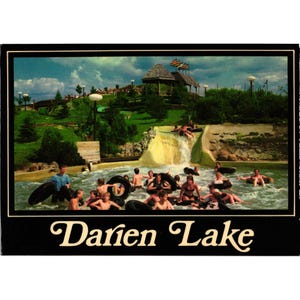Op de afbeelding: Vintage ansichtkaart met een waterparkscène in Darien Lake. Mensen drijven in binnenbanden in een zwembad met een waterval. Een houten prieel en weelderig groen zijn zichtbaar op de achtergrond. De lucht is bewolkt.