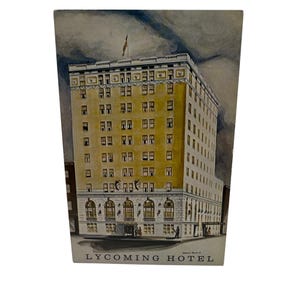 Puede incluir: Una postal vintage que representa un edificio de ladrillo amarillo con el texto "LYCOMING HOTEL" en la parte inferior. El edificio tiene muchas ventanas y un asta de bandera con una bandera estadounidense en la parte superior.