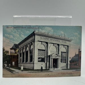 K&ouml;nnte beinhalten: Vintage Postkarte mit der Marine National Bank in Wildwood, N.J. Das Geb&auml;ude ist hellbeige mit gro&szlig;en Bogenfenstern und S&auml;ulen. Der Text "MARINE NATIONAL BANK" steht oben. Die Postkarte hat einen leichten Sepia-Ton.