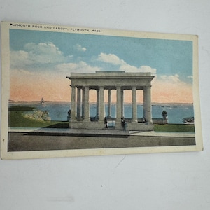 Op de afbeelding: Een vintage ansichtkaart met een afbeelding van Plymouth Rock en Canopy in Plymouth, Massachusetts. De ansichtkaart toont een witte stenen structuur met kolommen die uitkijken over een waterpartij. De lucht is lichtblauw met witte wolken.