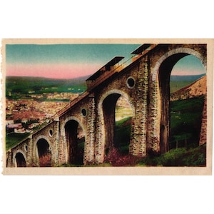 May include: Vintage postcard featuring a stone bridge with multiple arches, supporting a funicular railway. The bridge ascends towards the top of the image, with a city visible in the background. The sky transitions from pink to blue.
