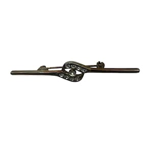 May include: A silver-toned brooch with a clear rhinestone design. The brooch is shaped like a stylized eye with a single larger rhinestone in the center.
