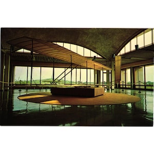 Puede incluir: Una postal antigua que muestra una exhibición de biplanos en un museo. La aeronave está suspendida en una gran sala con grandes ventanales. El suelo es reflectante y la iluminación es tenue.