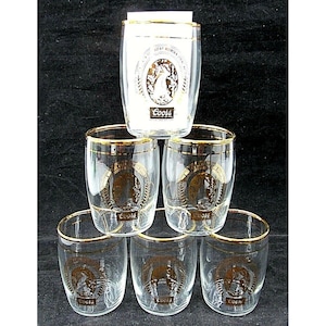 Puede incluir: Un juego de seis vasos de vidrio transparente con bordes dorados. Cada vaso presenta un emblema dorado con un caballo y la palabra "Coors". Un vaso está apilado encima de los demás. El vaso superior tiene un fondo blanco con las palabras "Rocky Mountain" y "Coors".