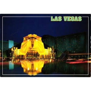 May include: A vintage postcard showing a night scene of a Las Vegas landmark. The image depicts a large, illuminated building with a lion's head facade, reflected in the water. The words "LAS VEGAS" are printed across the top.