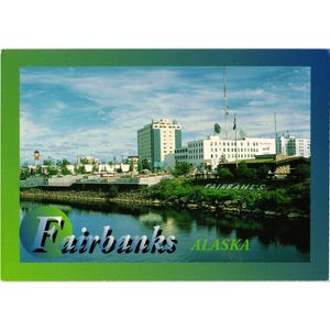 May include: A postcard featuring a scenic view of Fairbanks, Alaska. The image shows a river with buildings and a cloudy sky in the background. The word "Fairbanks" is prominently displayed, along with "Alaska". The postcard has a green and blue border.