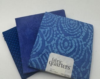Könnte beinhalten: Drei blaue Stoffpakete. Der Stoff hat verschiedene Muster, darunter ein kleines Punktmuster, eine einfarbige Farbe und ein Wirbeldesign. Das Etikett lautet "fabric quarters" und gibt die Größe mit 45 cm x 53 cm an.