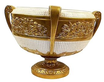 Puede incluir: Un gran cuenco de porcelana blanca con detalles dorados y elaborados. El cuenco tiene dos asas y se asienta sobre una base de pedestal. El cuenco está decorado con querubines y motivos florales.