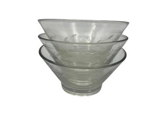 May include: Three clear glass bowls stacked on top of each other. The bowls have a flared shape and a delicate etched leaf design around the rim. The bowls are transparent, allowing light to pass through.