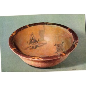 May include: A round, earthenware bowl with a reddish-brown rim and base. The interior is a light orange color with black geometric designs. The rim features alternating orange and brown triangles. The bowl has a rustic, handmade appearance.