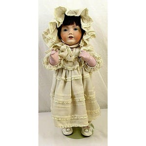 May include: A porcelain doll wearing a white dress with lace trim and a white bonnet. The doll has brown hair and blue eyes.