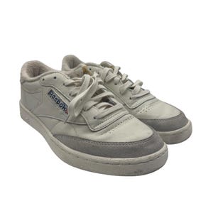 Op de afbeelding: Een paar witte leren Reebok Classic sneakers met een grijze suède neus en een witte rubberen zool. Het Reebok-logo is zichtbaar aan de zijkant van de schoen.