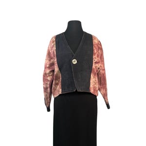 May include: A tie-dye style jacket with a black center panel and a single button closure. The jacket has a V-neck and long sleeves with black cuffs. The tie-dye pattern is a mix of pink and brown.