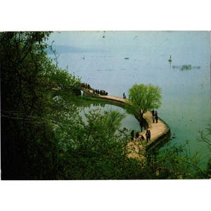 Pode incluir: Postal vintage com uma vista panorâmica de uma ponte de pedra sobre um lago. A ponte está repleta de pessoas, e uma árvore cresce nela. A água está calma e o céu está nublado.