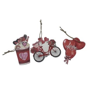May include: Three Valentine's Day wooden ornaments. One is a red coffee cup with a heart, another is a bicycle with hearts and flowers, and the last is two red hearts with the word "Love". All have glitter accents.