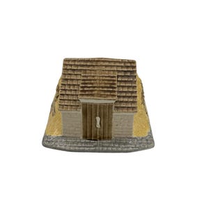 May include: A miniature ceramic church figurine. The roof is brown with a textured shingle design. The walls are beige with a wooden door. The base is gray with a stone pattern. The overall design is detailed and realistic.