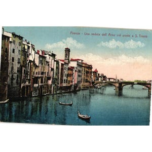 May include: Vintage postcard featuring a scenic view of Florence, Italy, with buildings lining the river and a bridge in the distance. The postcard has a blue and white sky, with boats on the water. The text "Firenze - Una veduta dell'Arno col ponte a S. Trinita" is visible.