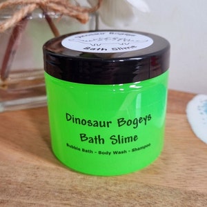 May include: A green jar of Dinosaur Bogeys Bath Slime. The jar has a black lid and a white label with the product name and description: "Bubble Bath - Body Wash - Shampoo".