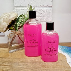 May include: Two clear plastic bottles of pink body wash with black lids. The bottles are labelled "Cottage Fresh Scents Snow Pixie Luxury Body Wash".