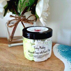 May include: A white jar with a black lid and a label that reads "Funky Monkey Whipped Soap with Kaolin Clay". The label also lists the scent notes: pear, orange, banana, strawberry, peach, raspberry, musk, creamy vanilla, and a hint of bubblegum.