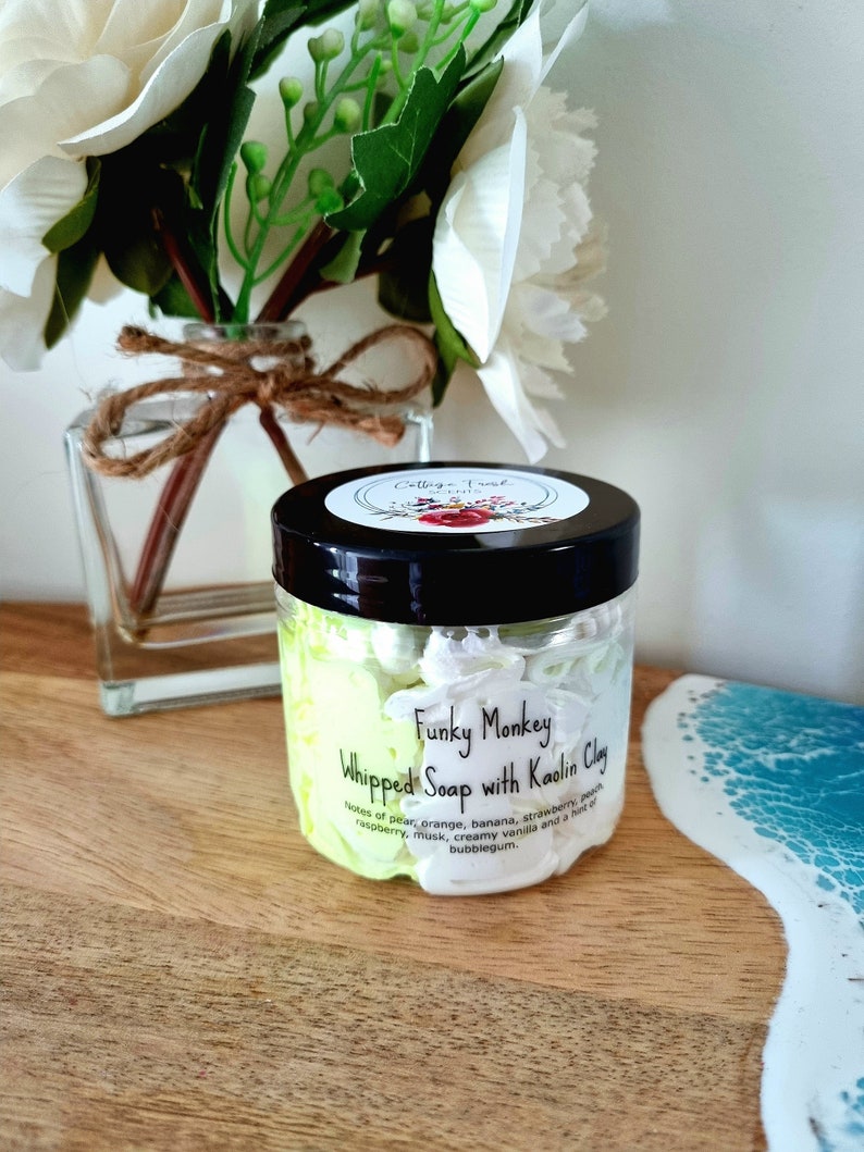 May include: A white jar with a black lid and a label that reads "Funky Monkey Whipped Soap with Kaolin Clay". The label also lists the scent notes: pear, orange, banana, strawberry, peach, raspberry, musk, creamy vanilla, and a hint of bubblegum.