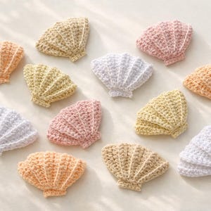 May include: A collection of twelve crocheted seashell appliques in various pastel colors including white, pale yellow, soft pink, and light orange. Each piece features a fan-shaped design with textured ridges radiating from a central base point.