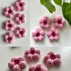 May include: A collection of pink crocheted flowers with a deep magenta center. The flowers are arranged in a cluster, showcasing their detailed petal design. The soft texture and vibrant colors create a charming, handmade aesthetic.