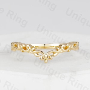 Può includere: Un delicato anello d'oro con un design delicato e intricato. L'anello è fatto di una fascia sottile con un design delicato e ornato che ricorda una corona o un motivo floreale.