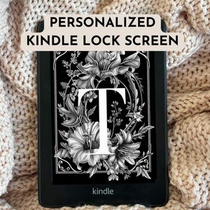 May include: A black Kindle e-reader displaying a personalized lock screen. The screen features a floral design with the letter "T" in white. The text "PERSONALIZED KINDLE LOCK SCREEN" is at the top. The e-reader rests on a beige knitted blanket.