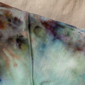 K&ouml;nnte beinhalten: Nahaufnahme eines Stoffes im Batik-Look in Blau-, Gr&uuml;n-, Lila- und Rosat&ouml;nen. Der Stoff ist ein weiches Material mit einer sichtbaren Naht, die durch die Mitte verl&auml;uft. Die Farben verschmelzen zu einem einzigartigen Muster.