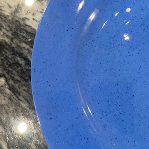 Puede incluir: Primer plano de un plato de cerámica azul con una textura moteada. El plato tiene un borde ligeramente elevado y un acabado brillante. El plato es de color azul vibrante.