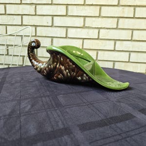 Może przedstawiać: Zielono-brązowa ceramiczna miska w kształcie rogu obfitości. Miska jest zaprojektowana tak, aby wyglądała jak róg z szerokim otworem na górze.