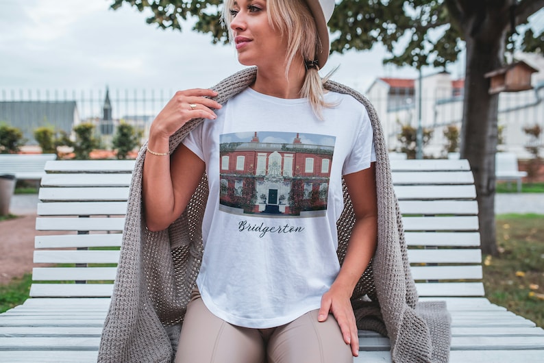 May include: White t-shirt with a printed image of a red brick building with a blue door and the text 'Bridgerton'.