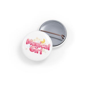 Könnte beinhalten: Zwei weiße, runde Ansteckbuttons. Einer zeigt den Text "Magical Girl" in Pink, mit einem Mond und Sternen. Der andere Button ist silberfarben mit einer Anstecknadel.