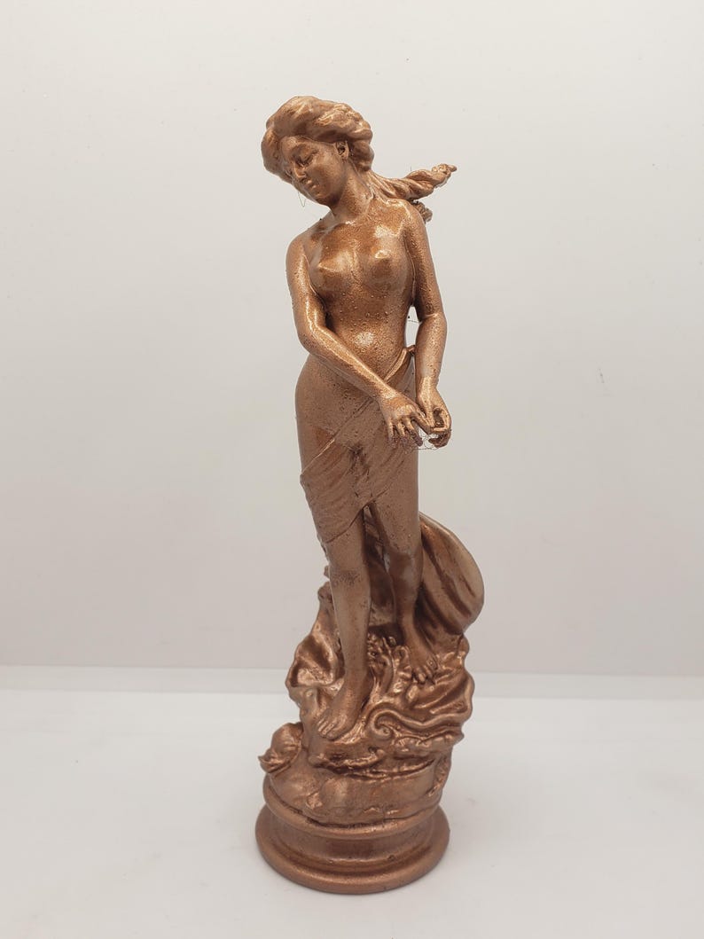May include: A copper-colored statue of a woman standing on a base with a flowing fabric draped around her. The statue is detailed with intricate carvings and a smooth finish.