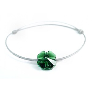 Pode incluir: Um bracelete com um fecho de trevo de cristal verde em um cordão cinza.