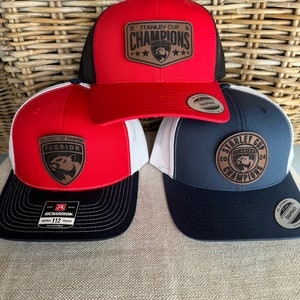 Può includere: Tre cappellini da baseball a tema Florida Panthers. I cappellini sono rossi, blu navy e neri con rete bianca. I cappellini hanno una toppa in pelle con il testo "2024 Stanley Cup Champions" e un logo di pantera. I cappellini sono regolabili con chiusura a scatto.