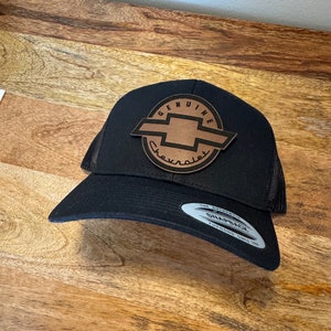 May include: Black mesh trucker hat with a brown leather patch featuring the Chevrolet logo and the text "Genuine Chevrolet".