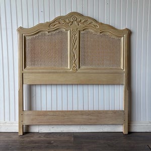 May include: A light wood headboard with a carved floral design and woven cane panels. The headboard has a simple, rectangular frame and a curved top.